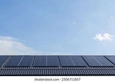 A solar panel array is installed on the roof of a building. The panels are angled to catch the sun's rays and convert them into electricity. The blue sky above the panels adds a sense of calm