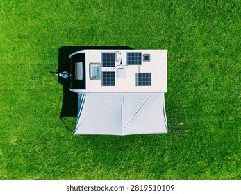 Solar panel array mounted on RV roof with awning set up on a vibrant green grassy field
