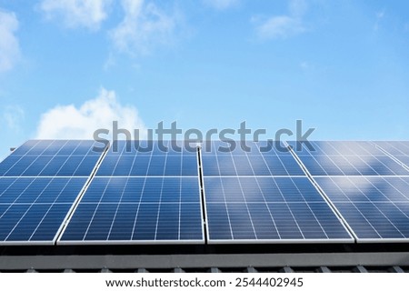 Solar panel cells on cloudy blue sky background. Clean alternative energy power concept. Modern house with solar panels stand-alone photovoltaic plant system on metal sheet roof. Go green