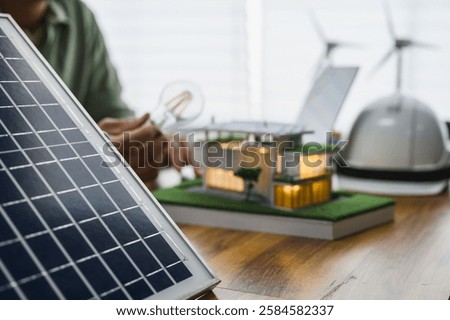 Solar panel example with Energy Design Engineer in background with an eco-friendly house model and wind turbines, symbolizing renewable energy and sustainable innovation, Innovation Development.