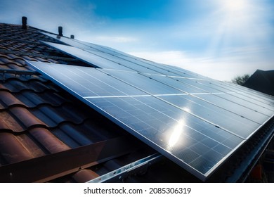 Solar panel on a red roof reflecting the sun and the cloudless blue sky - Shutterstock ID 2085306319