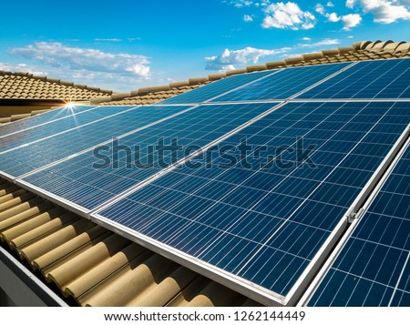 Solar panel on a red roof reflecting the sun and the cloudy blue sky in background