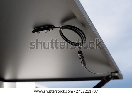 A solar panel sits installed on a home, showing the electrical connections visible from underneath. The area around features soft lighting with a simple background, providing space for additional text. The setup emphasizes renewable energy usage.
