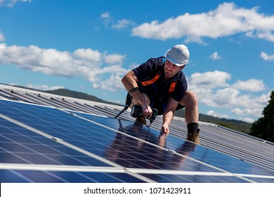 Solar panel technician with drill installing solar panels on roof on a sunny day