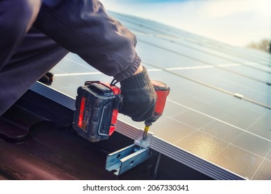 Solar panel technician with drill installing solar panels on roof.  technician in blue suit installing photovoltaic blue solar modules with screw. Electrician panel sun sustainable resources