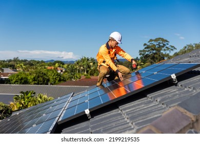 Solar panel technician with drill installing solar panels on house roof on a sunny day.