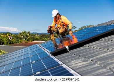 Solar panel technician with drill installing solar panels on house roof on a sunny day. - Shutterstock ID 2199594141