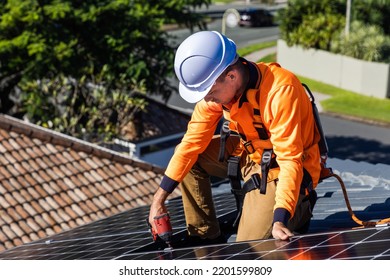 Solar Panel Technician With Drill Installing Solar Panels On House Roof On A Sunny Day.