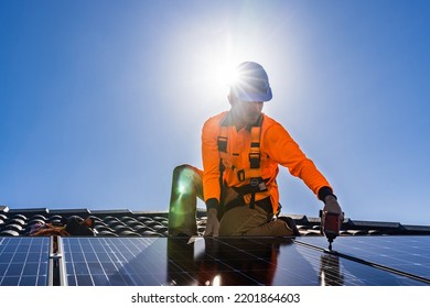 Solar Panel Technician With Drill Installing Solar Panels On House Roof On A Sunny Day.