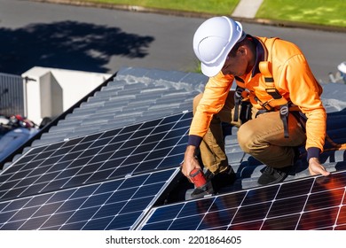 Solar Panel Technician With Drill Installing Solar Panels On House Roof On A Sunny Day.