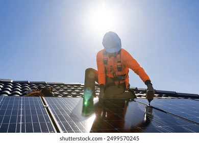 Solar panel technician with drill installing solar panels on house roof on a sunny day. - Powered by Shutterstock