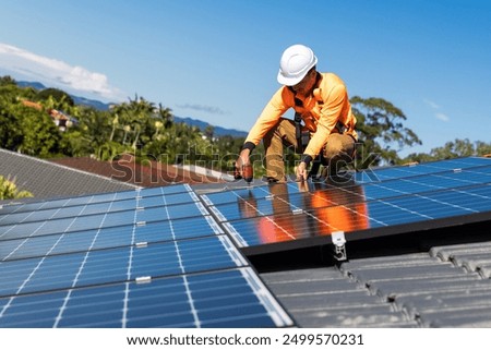 Solar panel technician with drill installing solar panels on house roof on a sunny day.