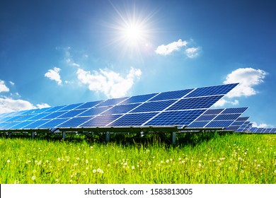 Solar Panel Under Blue Sky With Sun. Green Grass And Cloudy Sky. Alternative Energy Concept