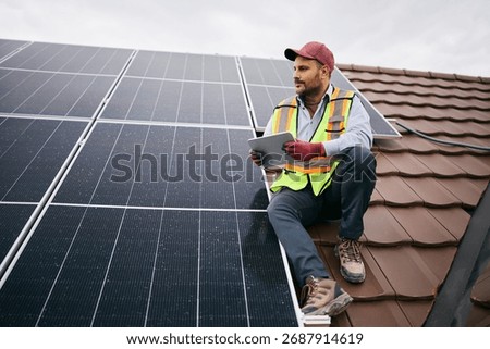 Solar panel worker using touchpad on the roof of a house. 