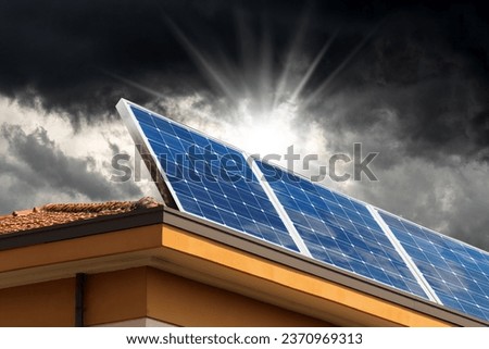 Solar panels above the roof of a house with storm clouds on background. Concept of low efficiency of renewable energy in adverse weather conditions.