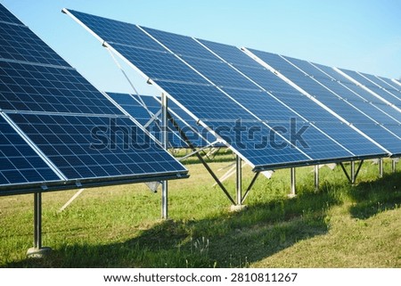 Solar panels converting sunlight into electricity, standing on a green field under a clear blue sky, demonstrating sustainable energy