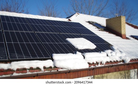 Solar Panels Covered By Snow. Photovoltaic Electricity Installation On The House Roof During Winter Season On A Sunny Day. Alternative Energy Home Production In Cold Weather.