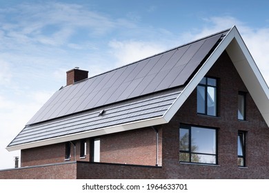 Solar panels mounted on the roof of a modern new-build house in a street in Heerenveen, Friesland, the Netherlands with sun and blue cloudy sky. Sustainable energy, electric power generation
