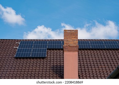 Solar Panels Mounted On The Rooftop Of A Residential House. Sunny Blue Sky, Brick Chimney, No People.