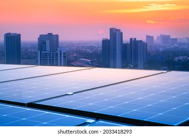 Solar Panels On The Rooftops Of Tall Buildings Reflect The Sunset. Modern Cities And Traffic Are The Backgrounds. Sustainable Renewable Energy. Modern Energy Concepts For Housing And Transportation