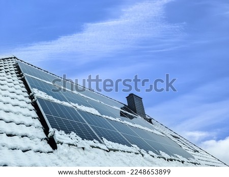 Solar panels producing clean energy on a snow coevered roof of a residential house