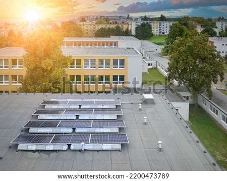 Solar power plant on the school roof. Aerial view of the photovoltaic panels against the school buildings and the city skyline, the setting sun, orange and blue.