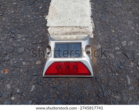 Solar Road Stud Reflective Marker Embedded in Asphalt Beside White Lane Line Detail