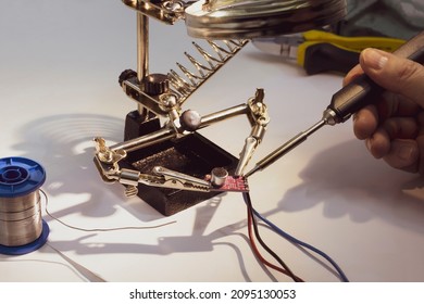 Soldering elements of printed circuit boards, soldering iron in hand. Soldering station, selective focus.