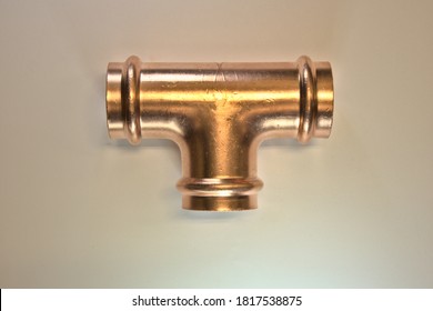 A solder-less crimp type copper  T plumbing fitting isolated against a white background