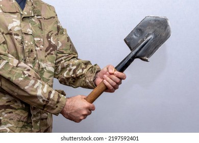 A Soldier In An American Military Uniform Holds A Sapper Shovel In His Hands On A Light Background.