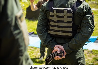 A Soldier In A Bulletproof Vest Holds A Magazine With Cartridges Behind His Back. Back View