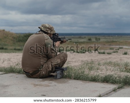 A soldier in a bush hat fires from the sitting position at a military range, storm clouds massing over the open training area.