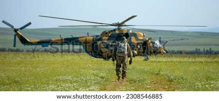A soldier in camouflage goes to a military helicopter. Military helicopter with soldiers. Armed conflict, hostilities. Air armament, parachutist.