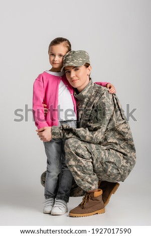Soldier embracing daughter and looking at camera on grey background 