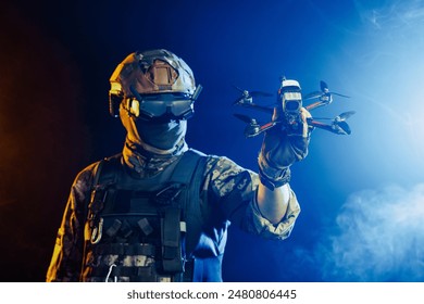 Soldier in gear holds drone against a red and blue smoky background, conveying intensity and military action - Powered by Shutterstock