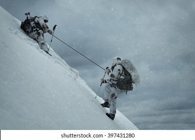 Soldier Helping Another To Climb Up The Hill. Two Military Men In The Background Of A Winter Landscape