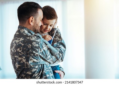 Soldier And His Little Son Hugging At Home. Smiling Soldier Reunited With His Son After Coming Back From War. Military Soldier Father With Son Kid Smiling During Home Return - Family Love US Army