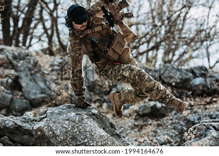 Soldier jumping over a rock in full gear. Simulated battle