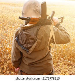 A soldier with a machine gun stands in a field, Ukrainian wheat fields and war, a woman warrior with a machine gun.
