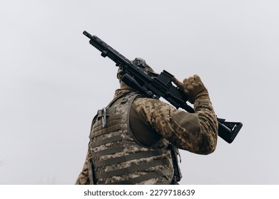 A soldier with a machine gun stands with his back in military uniform