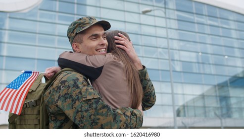 Soldier man in camouflage uniform standing and embracing his loved one. Portrait of happy couple with romantic reunion. Soldier hugging wife with american flag in her hand. Crop view - Powered by Shutterstock