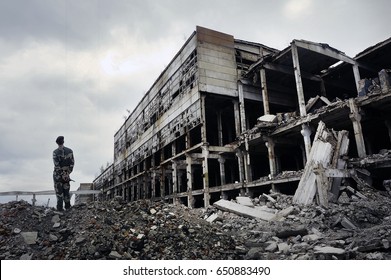 Soldier in military uniform stands on the ruins of the destroyed house. Hot spots on the planet. The concept of the fight against terrorism.