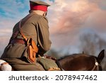 Soldier on horseback in rear view against a sky with apricot colored clouds.