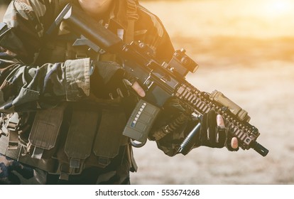 The soldier in the performance of tasks in camouflage and protective gloves, holding a gun. The zone of military operations.
