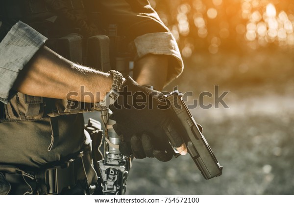 the soldier in the performance of tasks in camouflage and protective gloves holding a pistol. War Zone.