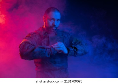 Soldier In The Studio On A Blue Background. A Man In Military Uniform With A Rifle Or Machine Gun In Colored Light And Smoke. Military Or Airball Player. Blur