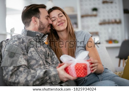 Soldier surprising his wife with a gift. Young man giving gift box to his girlfriend..	