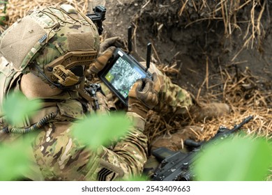 Un soldado con equipo táctico opera una tableta de control en el campo, utilizando tecnología para el reconocimiento con una pantalla de vista Aéreas.