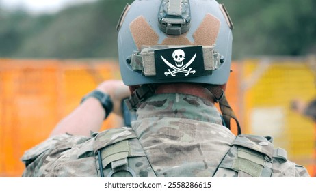 Soldier with Tactical Helmet and Skull Patch. A soldier in camouflage gear wearing a tactical helmet with a skull and crossbones patch during a military training exercise. - Powered by Shutterstock