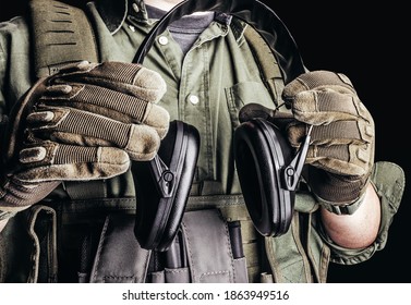 Soldier in tactical outfit with body armor, gloves and shirt holding shooting earmuffs on black background. - Powered by Shutterstock